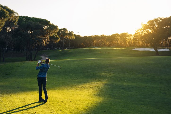 Male golf player teeing off golf ball from tee box to beautiful sunset