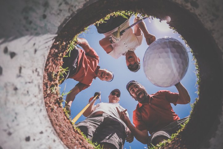 A Point Of View picture of 4 Golf Players and Golf Ball view From Inside the Hole on a sunny day of summer. The players are excited and happy.